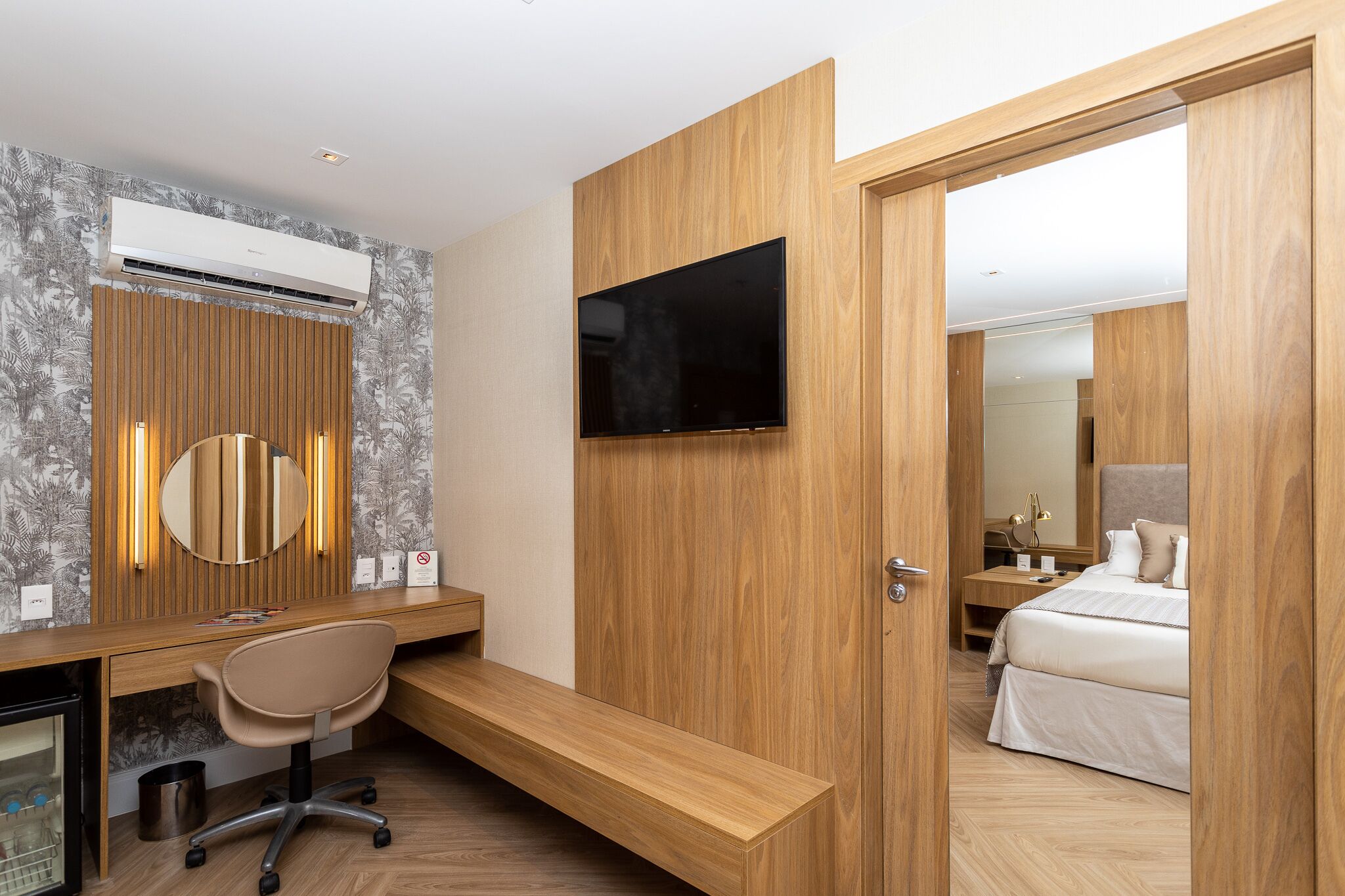 Een moderne hotelkamer met een houten bureau, een televisie, een bed en een spiegel.
