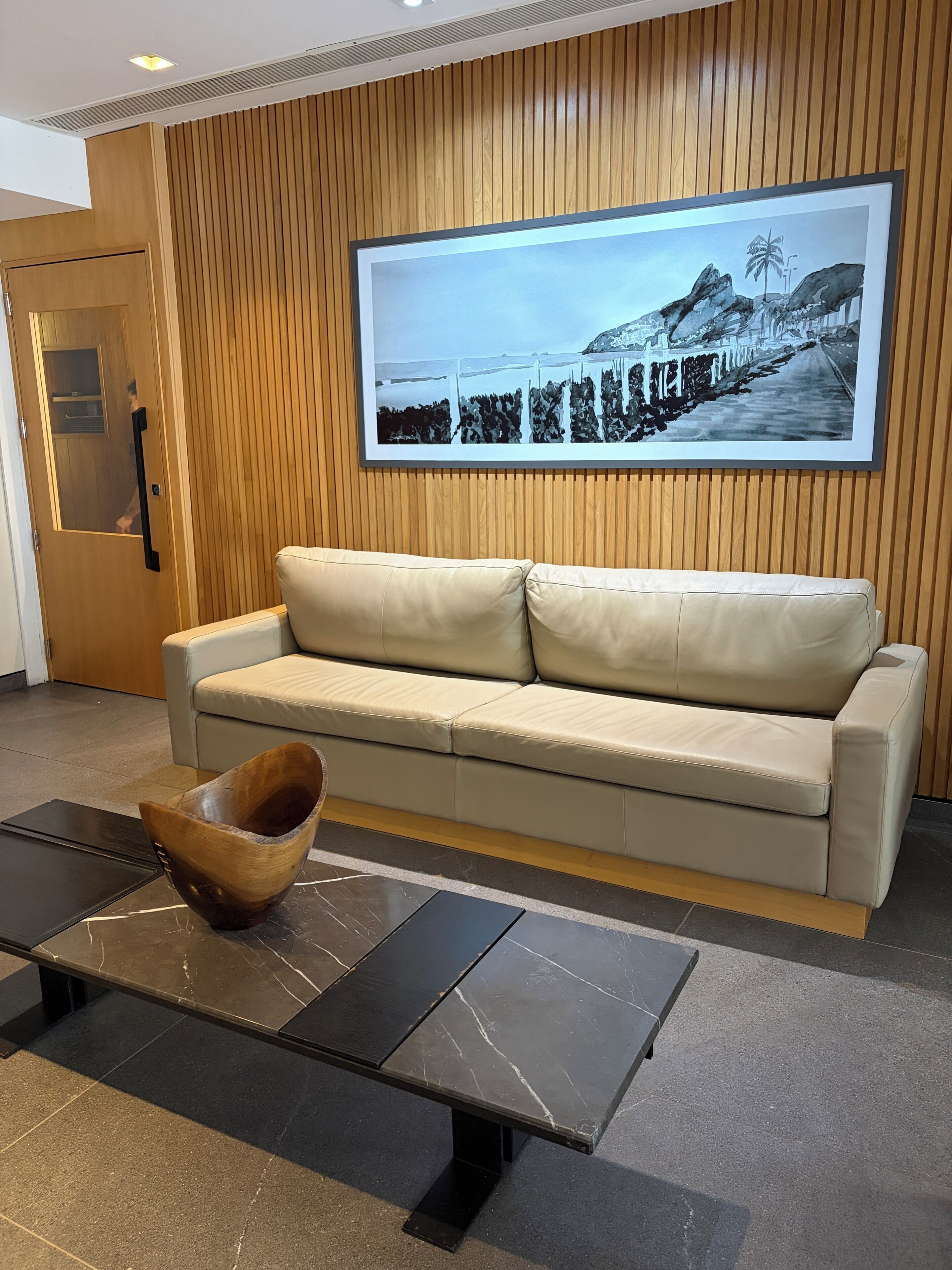 A modern lobby with a beige leather sofa, a wooden bowl on a black table, and a large framed picture on the wall.