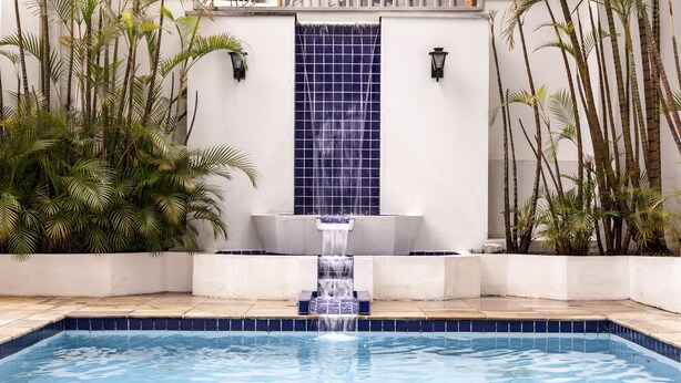 Une piscine agrémentée d’une cascade, entourée de plantes tropicales et bordée d’un mur recouvert de carreaux.