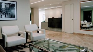 Un hall d’entrée moderne avec deux fauteuils blancs, un comptoir d’accueil et un grand miroir qui reflète l’intérieur.