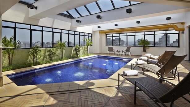 A rooftop pool area with a view of the city, sun loungers, and a tiled floor.