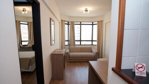 A hotel room with a bed, a sofa, a desk, and a window with curtains. There is a sign indicating no smoking. - L'Hirondelle Flat Service (Campinas)