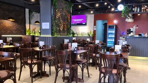 A restaurant interior with multiple tables and chairs, a bar area with a counter and shelves of bottles, and a digital menu display. - L'Hirondelle Flat Service (Campinas)
