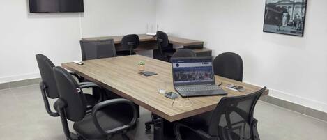 Una sala de conferencias con una mesa larga, cuatro sillas, una computadora portátil y un cuadro en la pared.