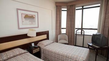 A hotel room with two beds, a chair, a television, and a window with curtains.