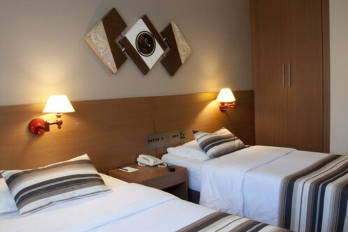 A hotel room with two beds, a wooden headboard, bedside lamps, a telephone, and a wall-mounted artwork.