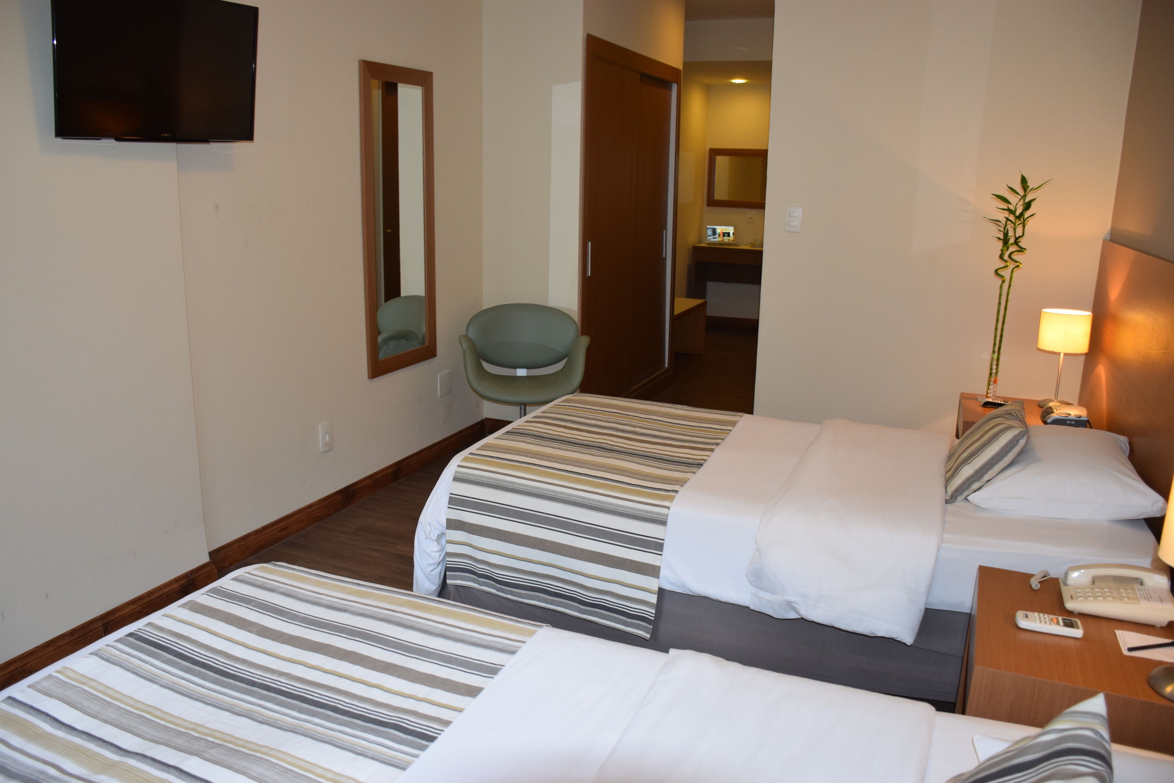 A hotel room with two beds, a TV, a desk with a phone, a chair, and a bathroom visible in the background.