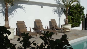 Uma área na beira da piscina com espreguiçadeiras e plantas em vasos.