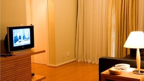 Een hotelkamer met een televisie op een houten standaard, een lamp op een bijzettafeltje en een zwarte bank.