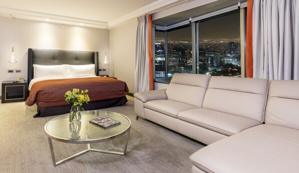 A hotel room with a bed, a sofa, a glass coffee table, and a view of a cityscape at night. - InterContinental Santiago by IHG (Santiago)
