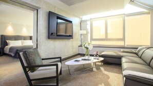 Ein modernes Hotelzimmer mit einem großen Bett, einer Couch, einem Sessel, einem Couchtisch und einem an der Wand befestigten Fernseher.
