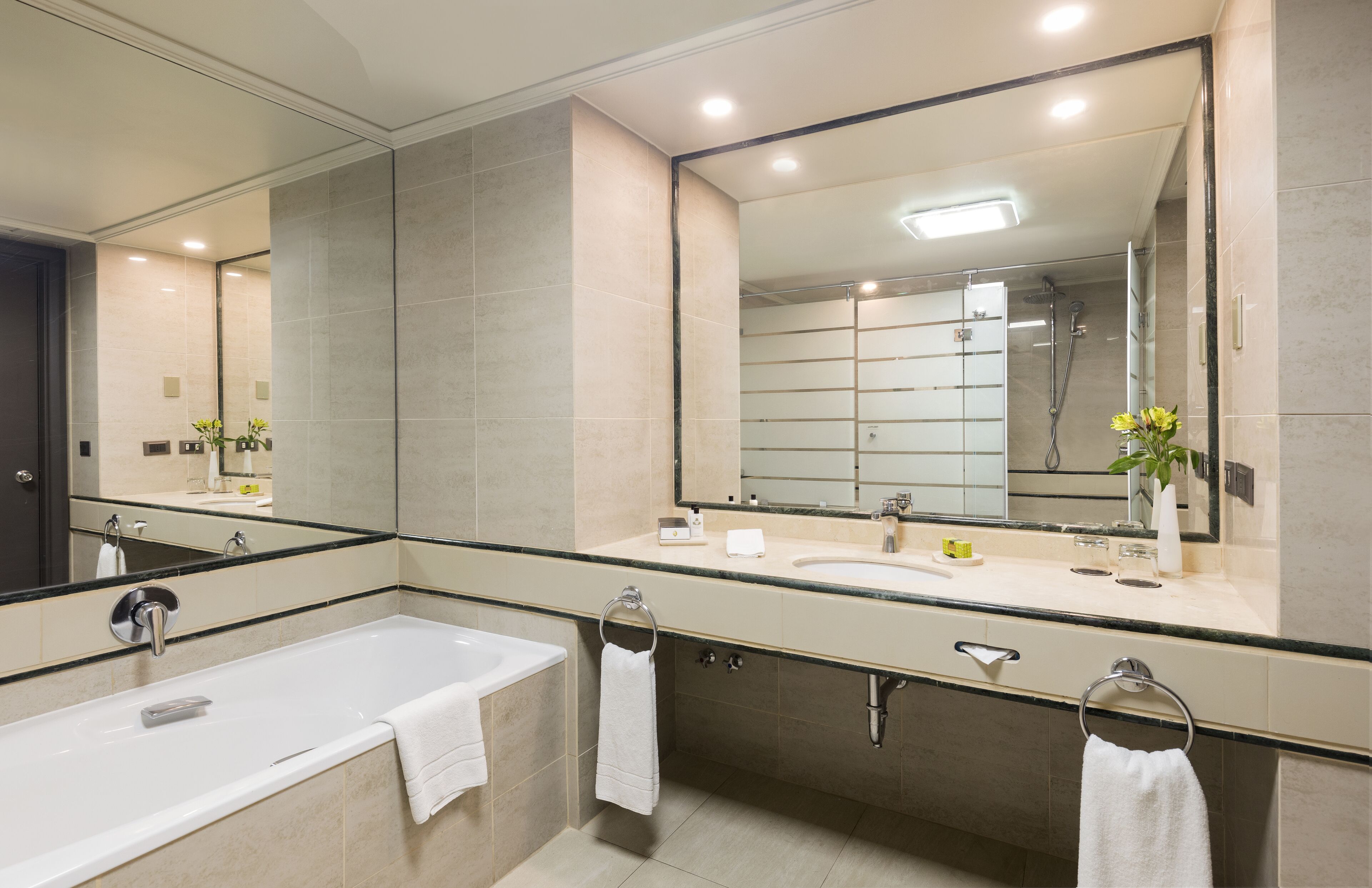 A modern bathroom with a large mirror, a bathtub, a sink, and a shower.