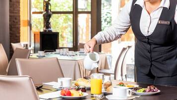 A hotel dining area with a waiter pouring coffee into a cup, breakfast plates with fruit and pastries, and a view of the outdoors through large windows.