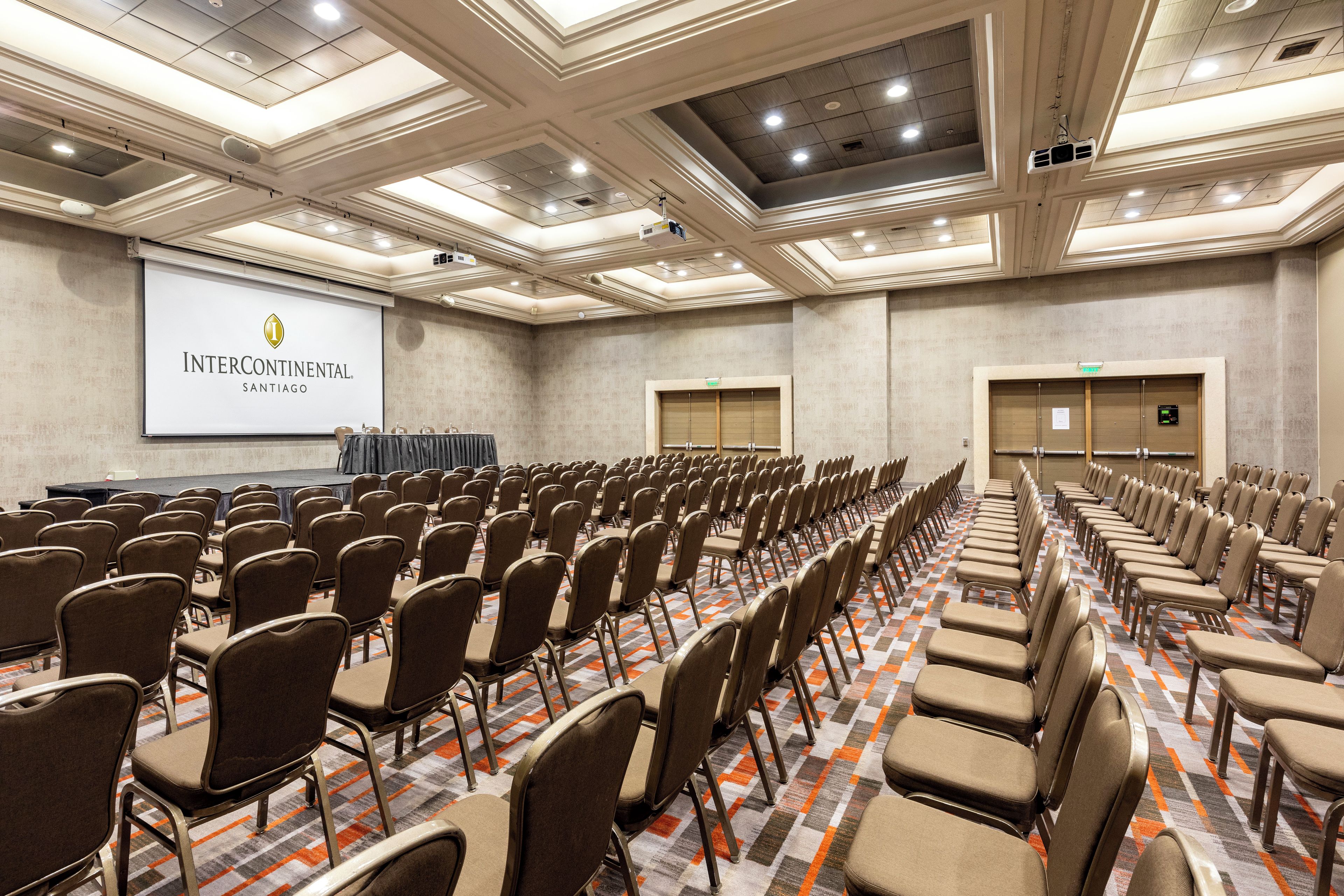 A conference room with rows of chairs, a projection screen, and a stage.