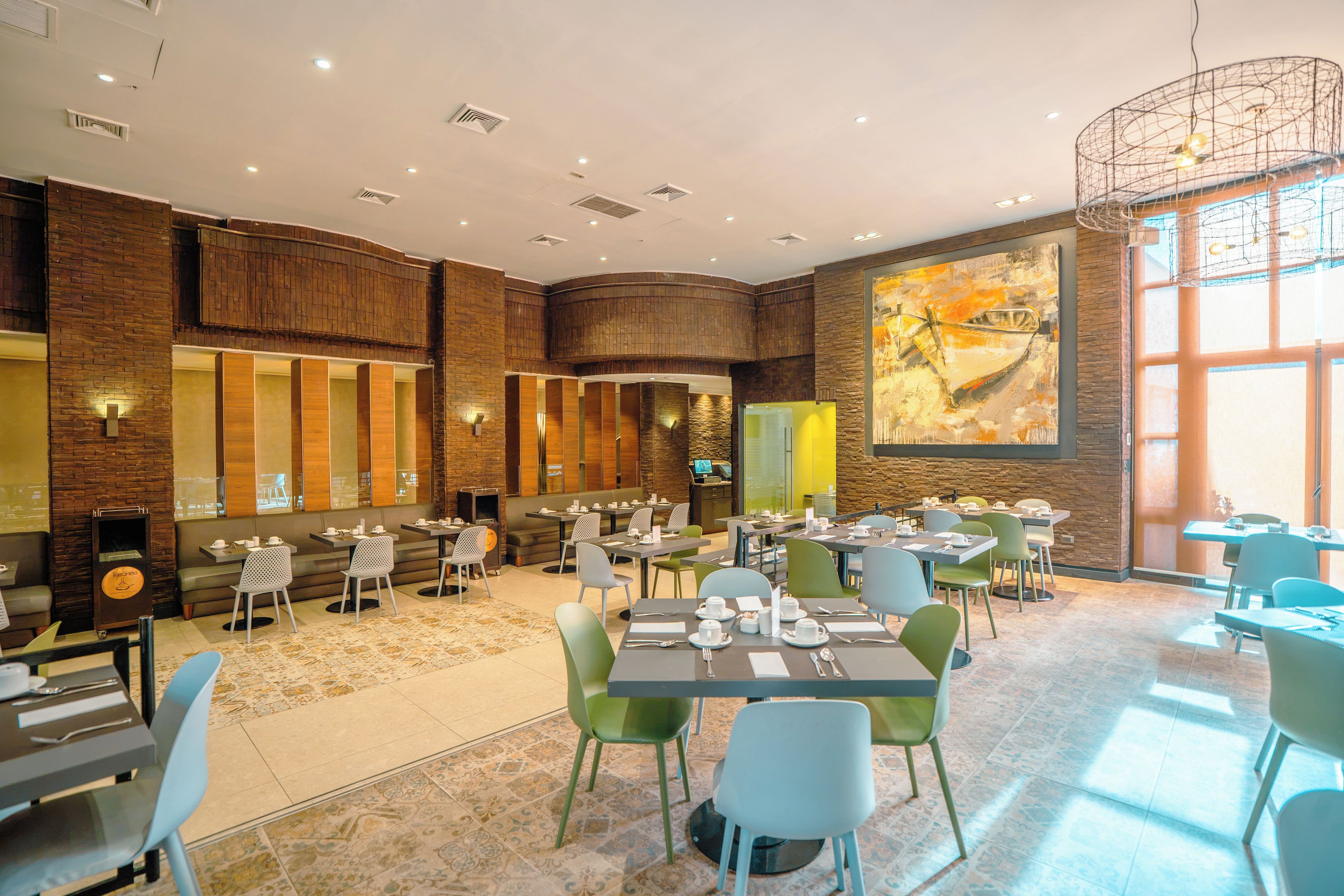A spacious dining area with multiple tables and chairs, a large painting on the wall, and a brick wall design.