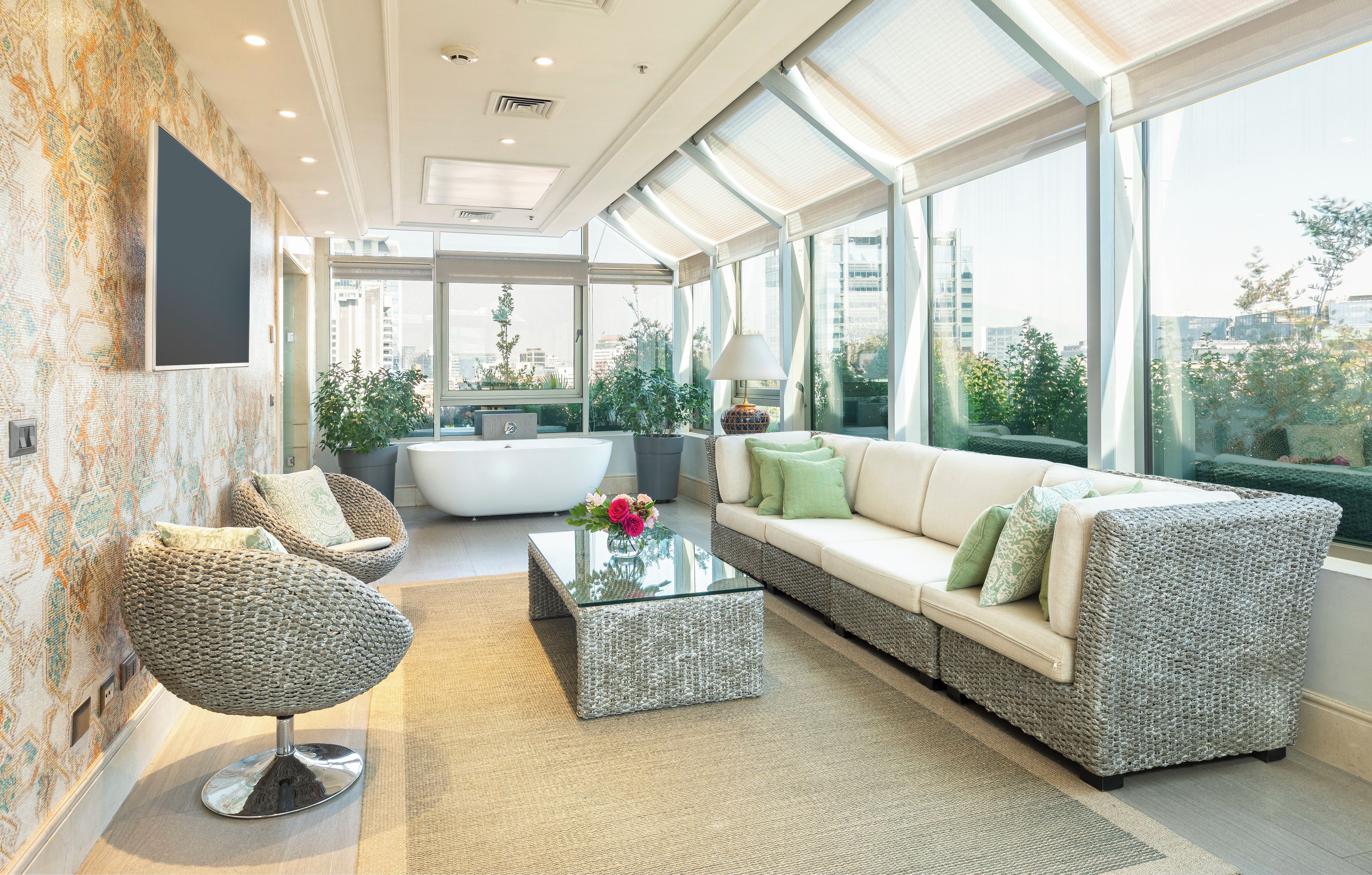 A modern living room with a sofa, armchair, and coffee table, large windows with city views, and a patterned wall.