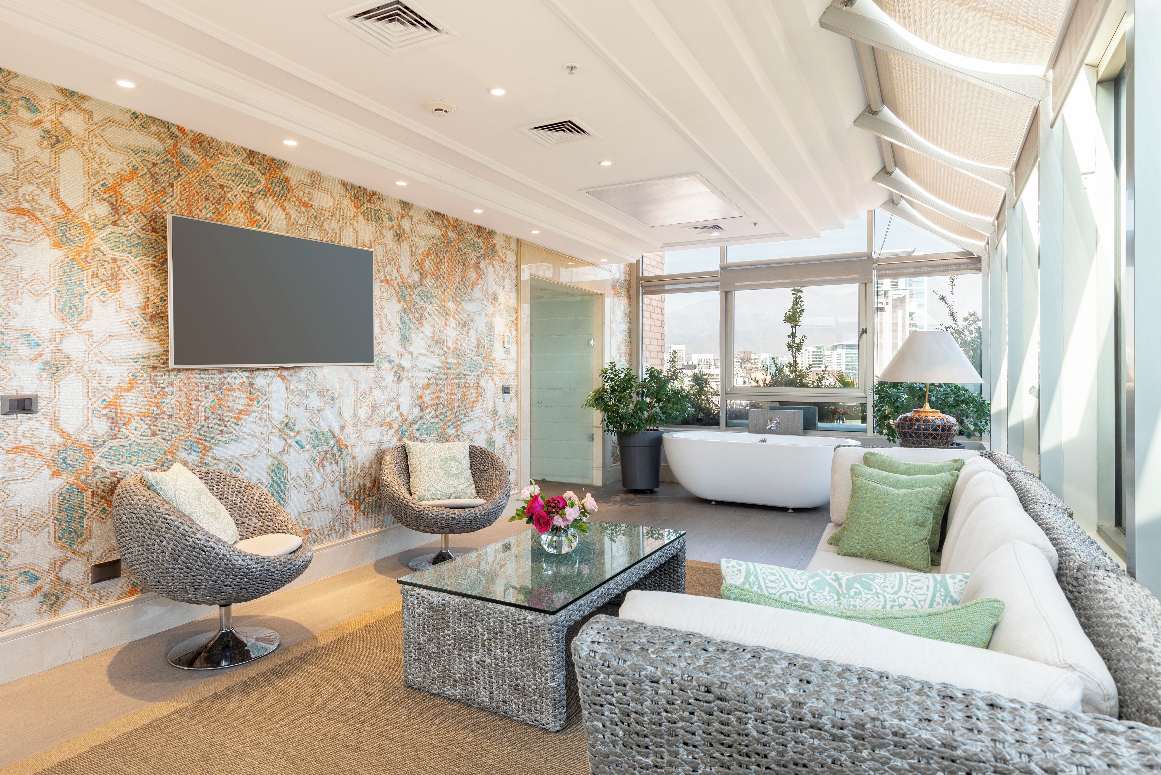 A modern living room with a sofa, two armchairs, a glass coffee table, and a flat-screen TV mounted on the wall.