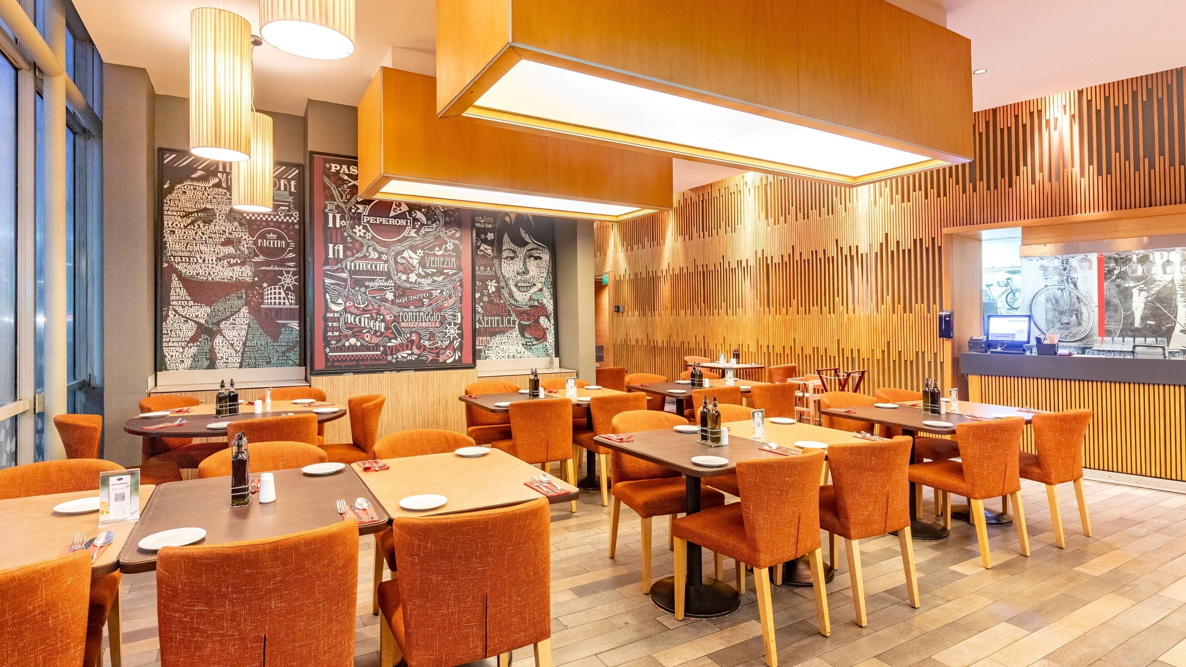 Ein Restaurantinneres mit mehreren Tischen und orangefarbenen Stühlen, Holzvertäfelung an den Wänden und gerahmten Kunstwerken.