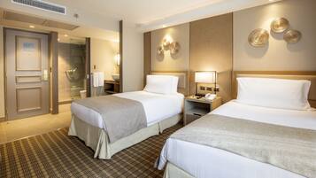 A hotel room with two beds, a bathroom with a glass shower, and a wall-mounted phone.