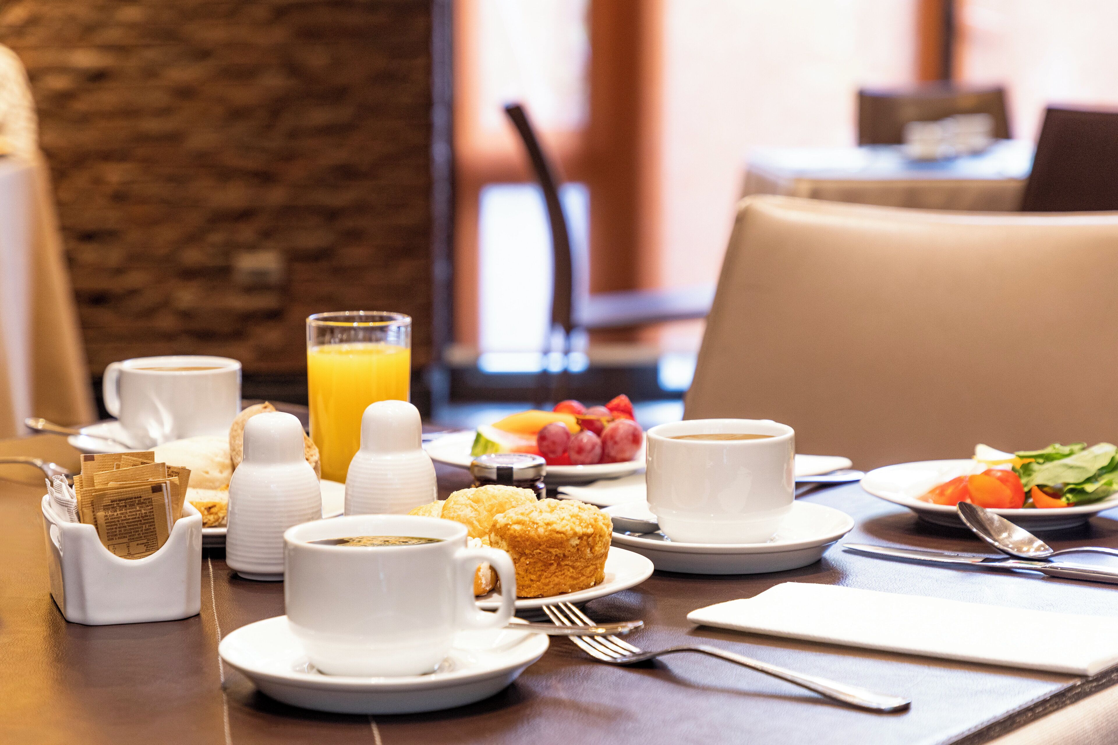 A breakfast setting with coffee, juice, pastries, and fruit on a table.