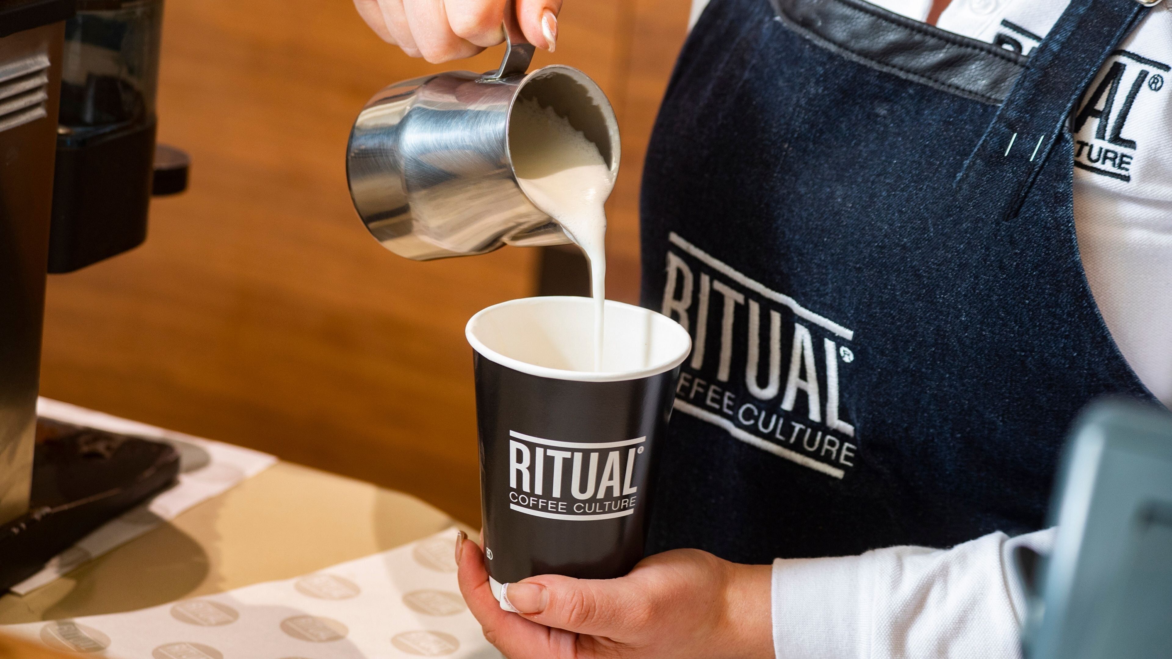 A person pouring milk into a coffee cup labeled "RITUAL COFFEE CULTURE".