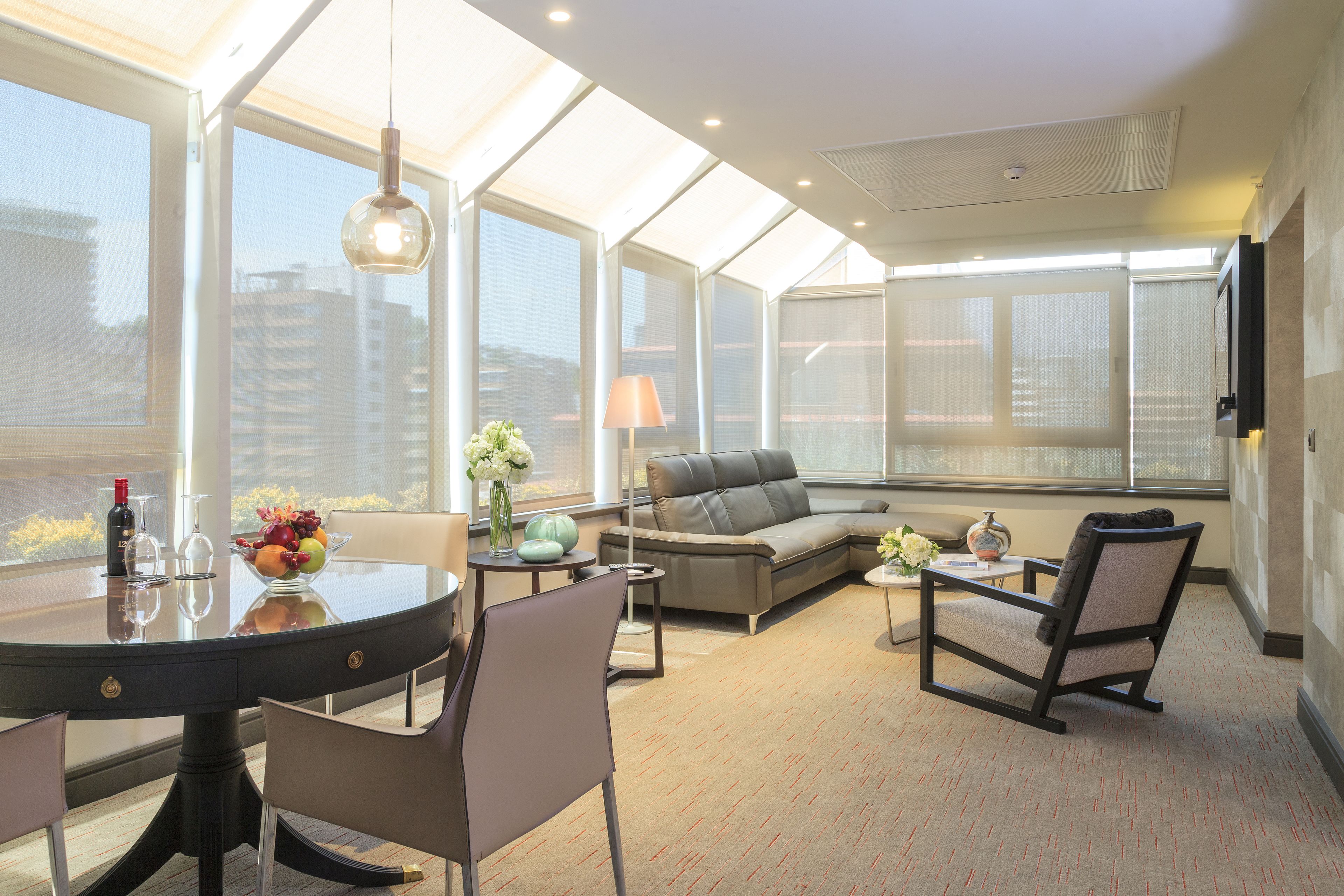 A modern living room with a glass ceiling, a dining table, chairs, a sofa, and a TV mounted on the wall.