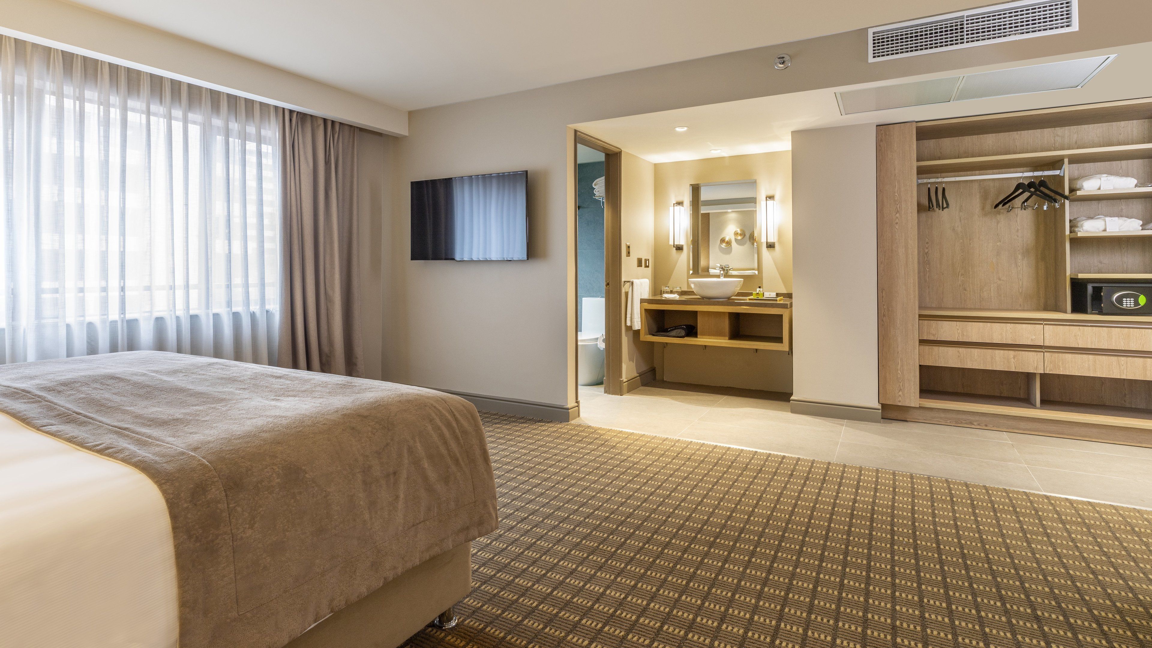 A hotel room with a bed, a bathroom with a sink and mirror, and a walk-in closet with hangers.