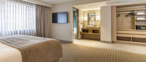 Habitación de hotel con cama, baño con lavamanos y espejo, y vestidor con perchas.