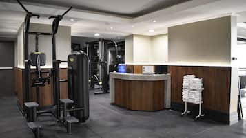 Uma academia com diversos equipamentos de exercício, uma mesa de recepção e um suporte para toalhas.