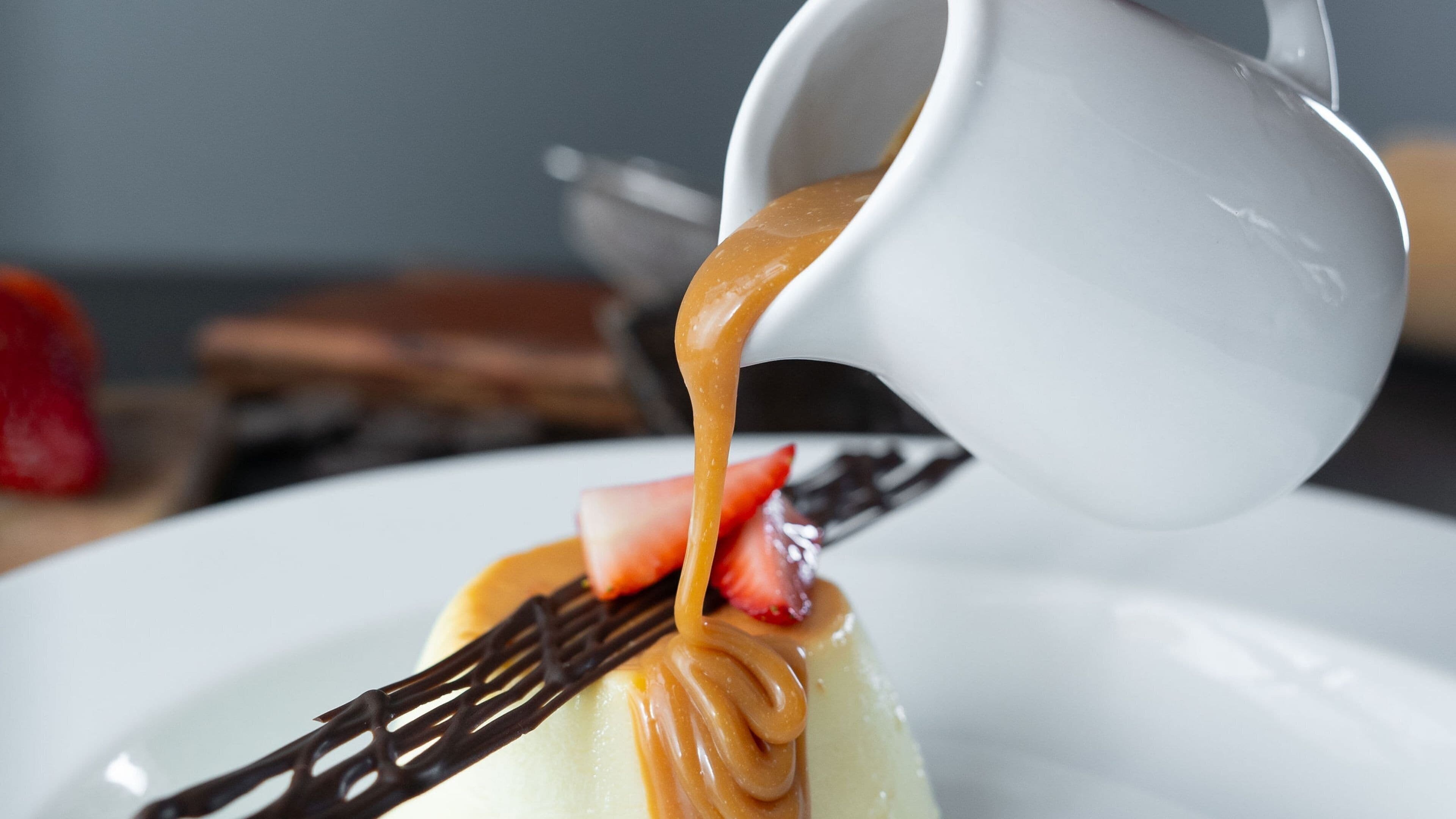 A dessert with caramel sauce being poured over a white plate with a fork.
