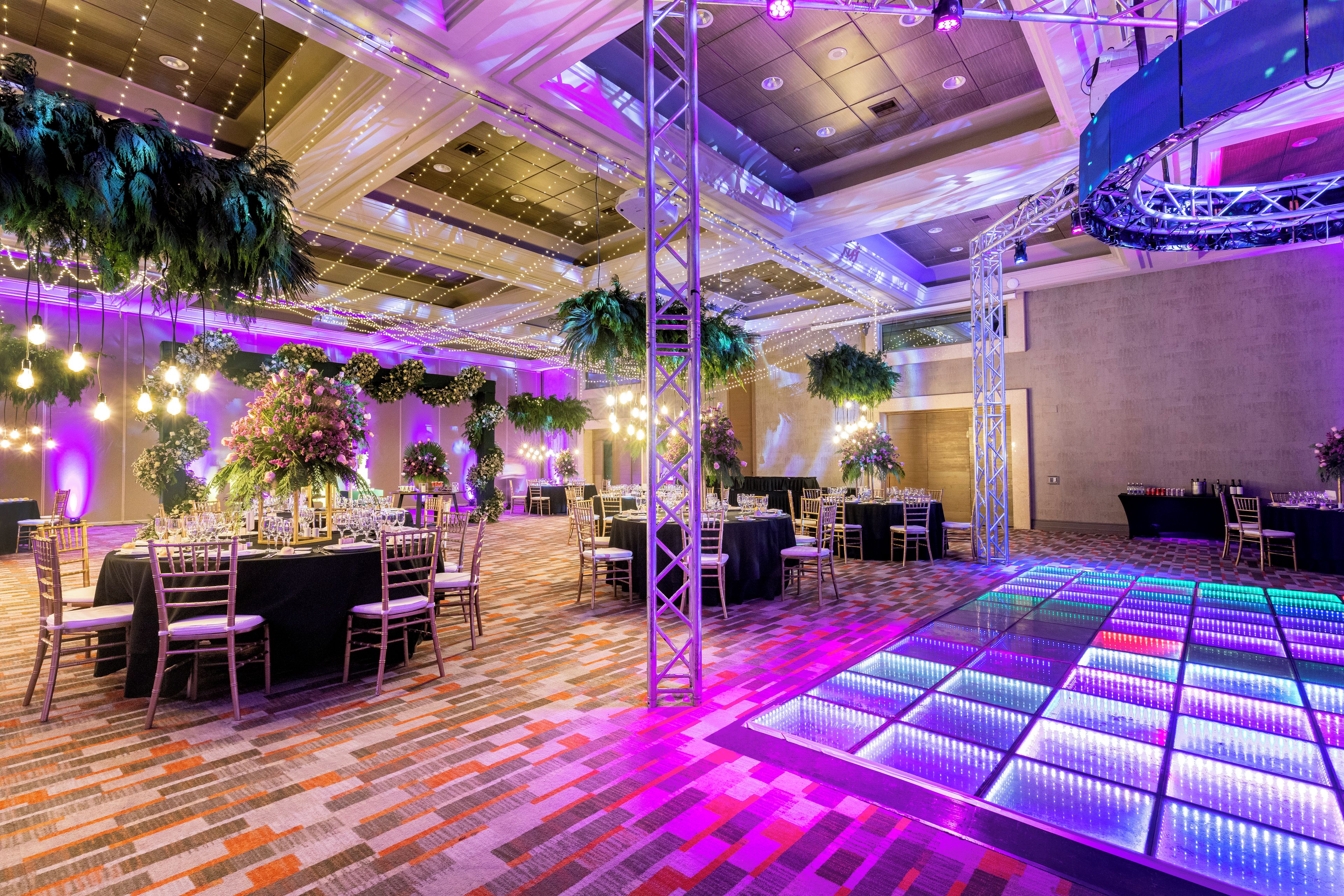 Un espace intérieur spacieux, aménagé avec des tables pour les repas, une piste de danse dotée d’un éclairage à LED et agrémenté de plantes décoratives.