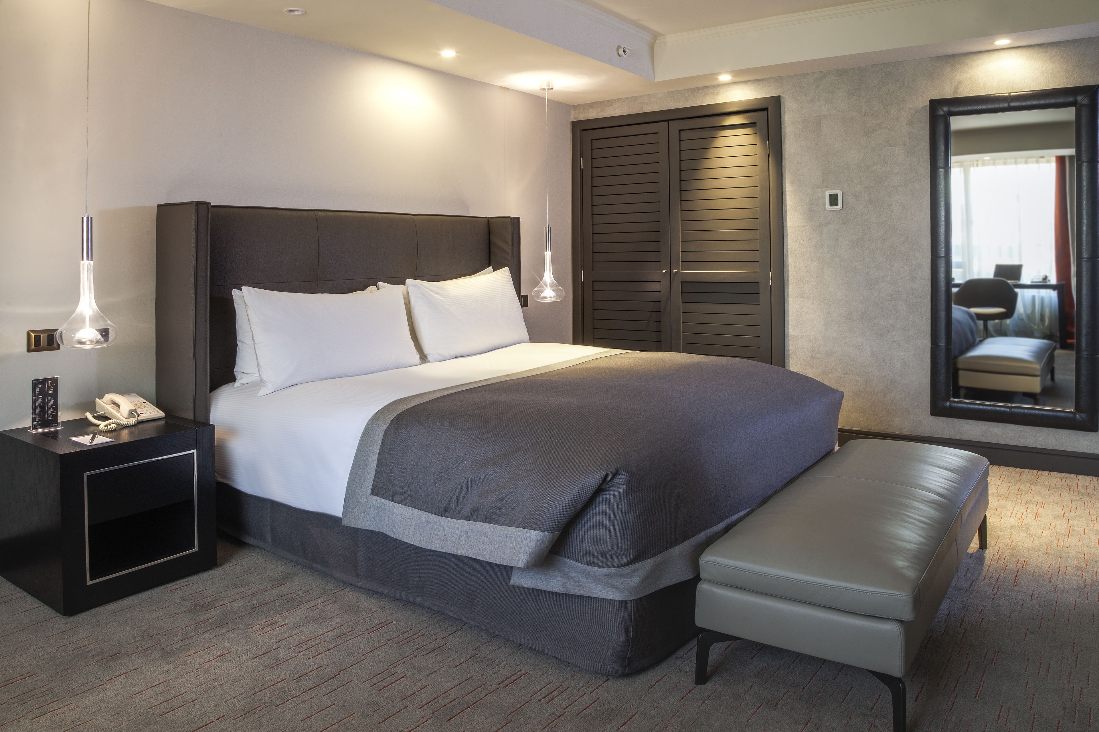 Una habitación de hotel moderna con una cama grande, mesitas de noche, un banco y un espejo.