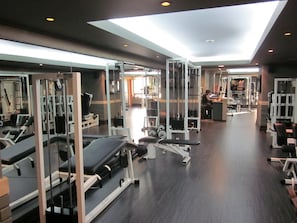 Un gimnasio con diverso equipamiento de ejercicio, paredes con espejos y tragaluces.