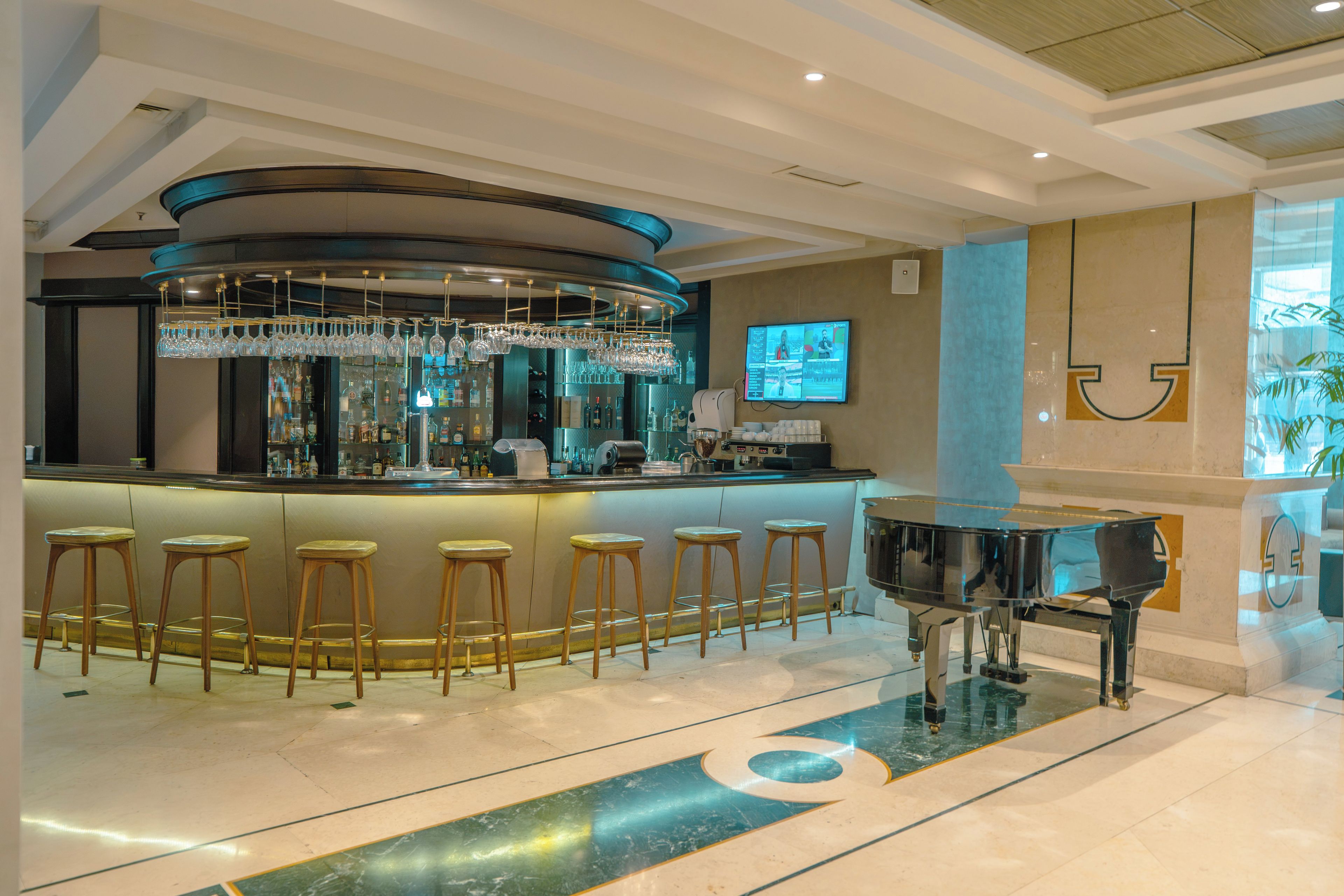 Zona de bar con un piano, taburetes y una barra con vitrina de vidrio.