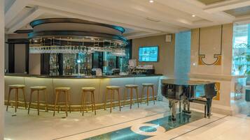 Zona de bar con un piano, taburetes y una barra con vitrina de vidrio.
