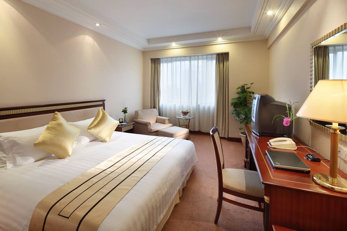 A hotel room with a large bed, a desk with a telephone, a laptop, and a television.