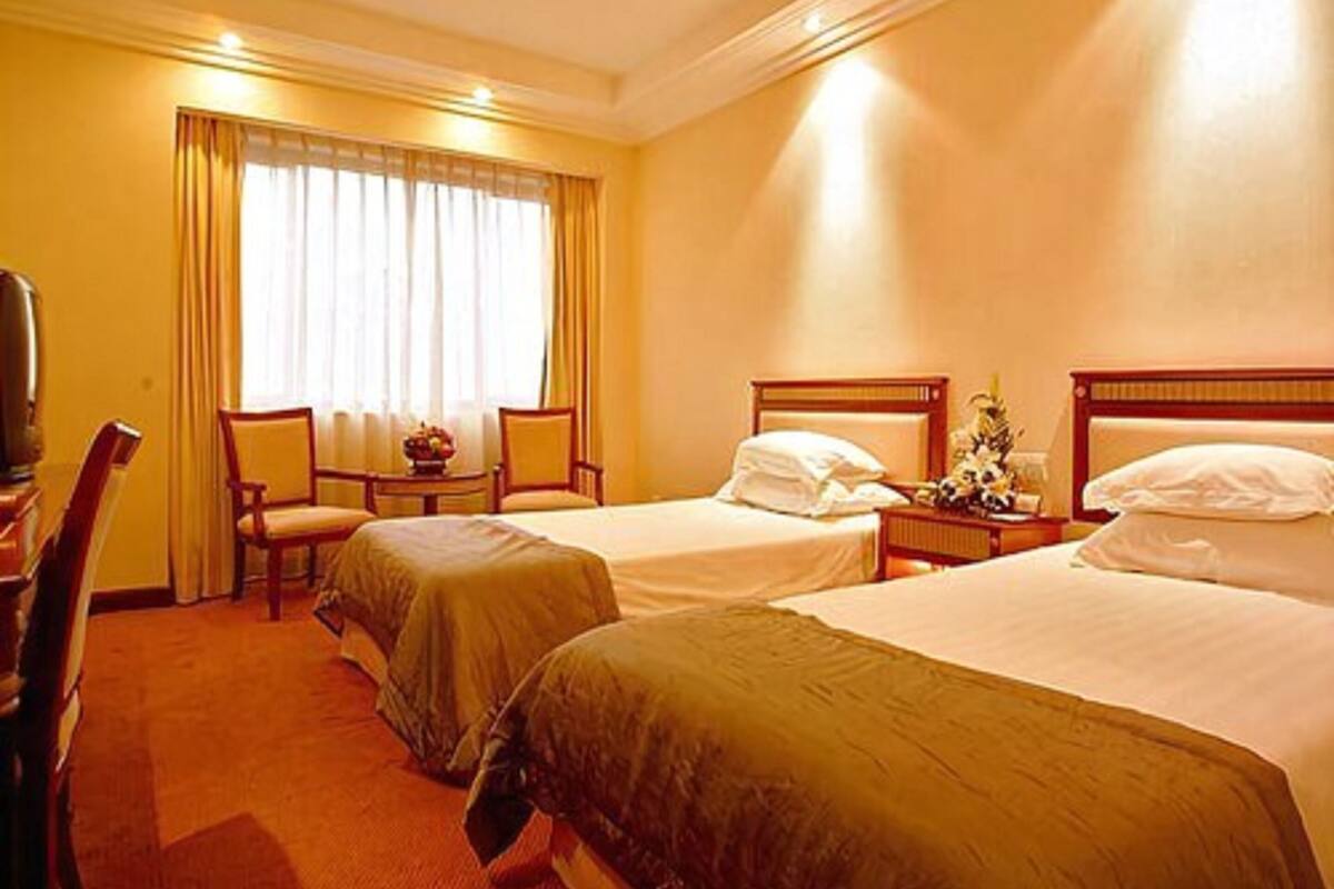 A hotel room with two single beds, a desk, a chair, and a television.