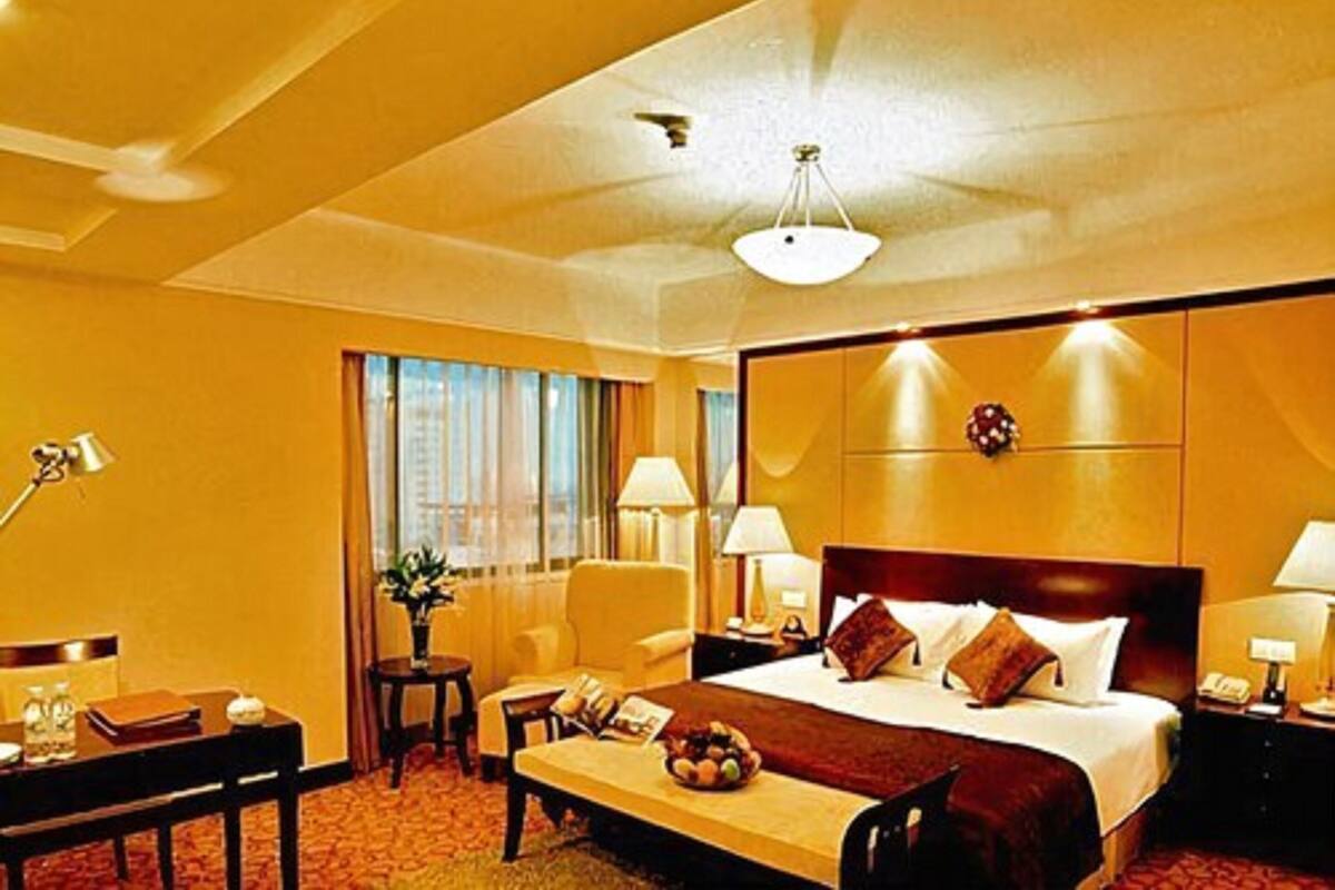 A hotel room with a large bed, bedside lamps, a desk with a chair, and a small table with a bowl of fruit.
