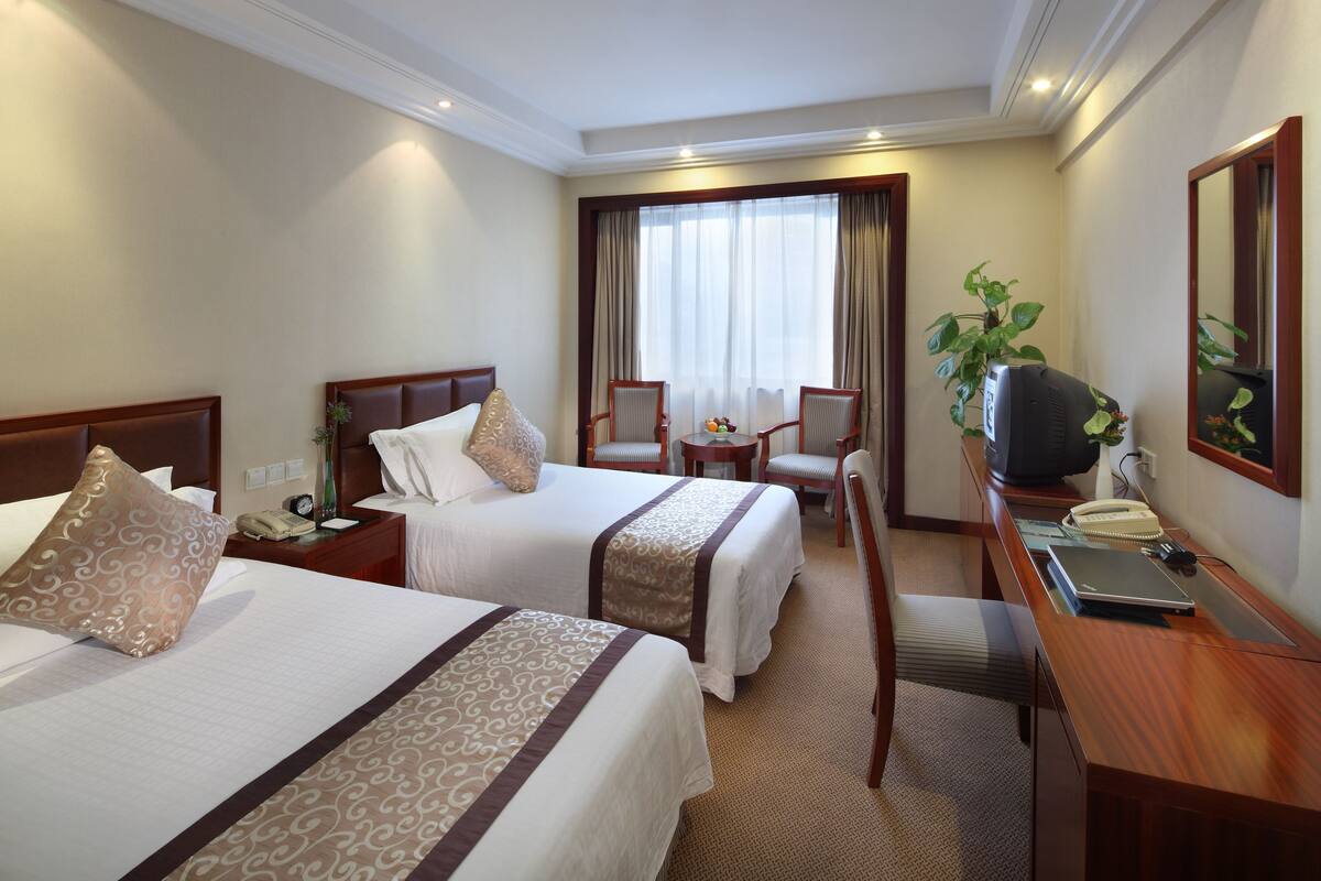 A hotel room with two beds, a desk, a chair, a TV, and a window with curtains.