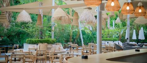 An outdoor seating area with wicker furniture and thatched umbrellas, surrounded by lush greenery.