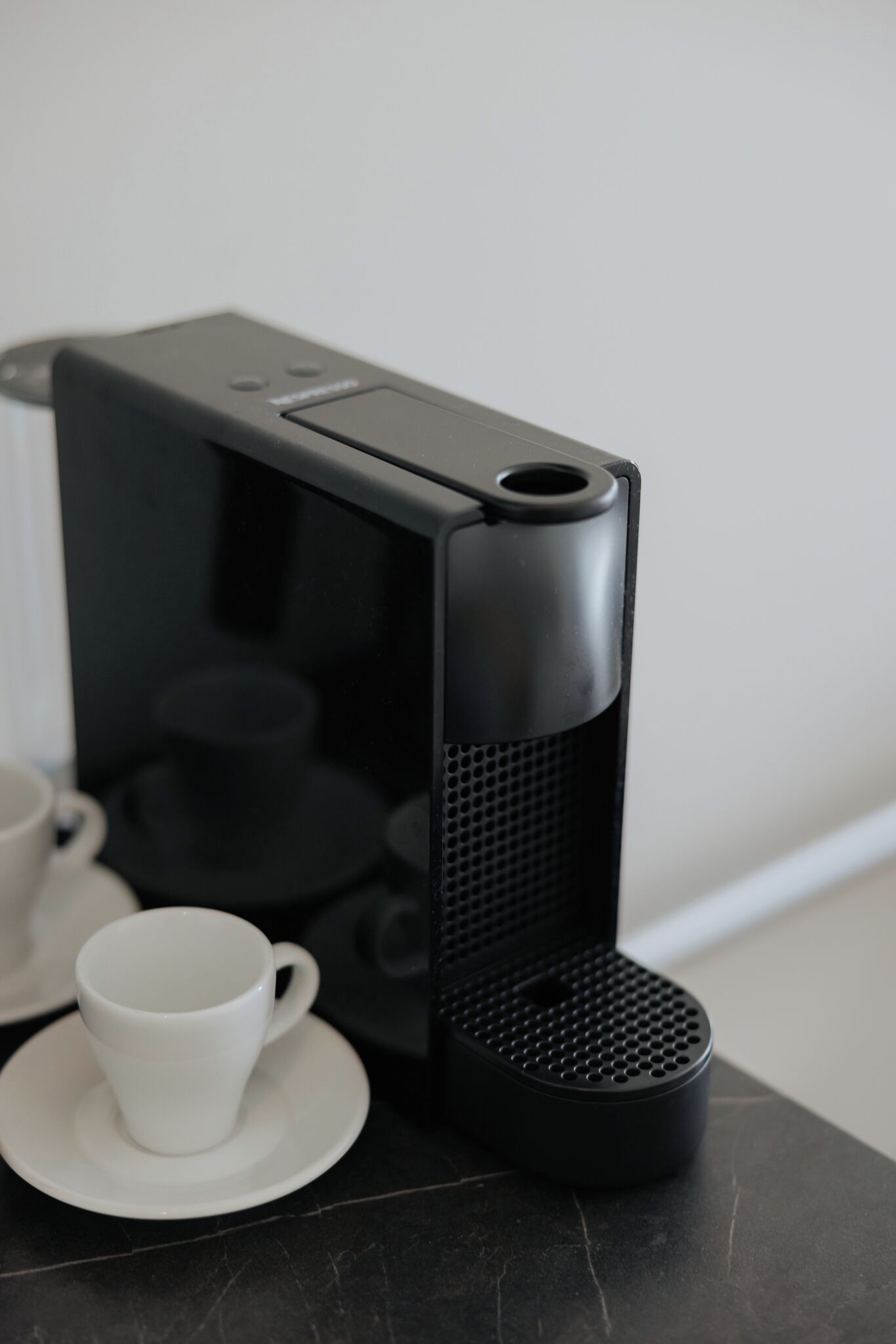 Una caffettiera nera su un piano di marmo scuro, con una tazza e un piattino bianchi nelle vicinanze.