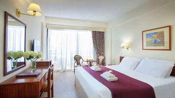 Ein Hotelzimmer mit Bett, Schreibtisch, Stuhl, Tisch mit Blumenvase und einem Gemälde an der Wand.