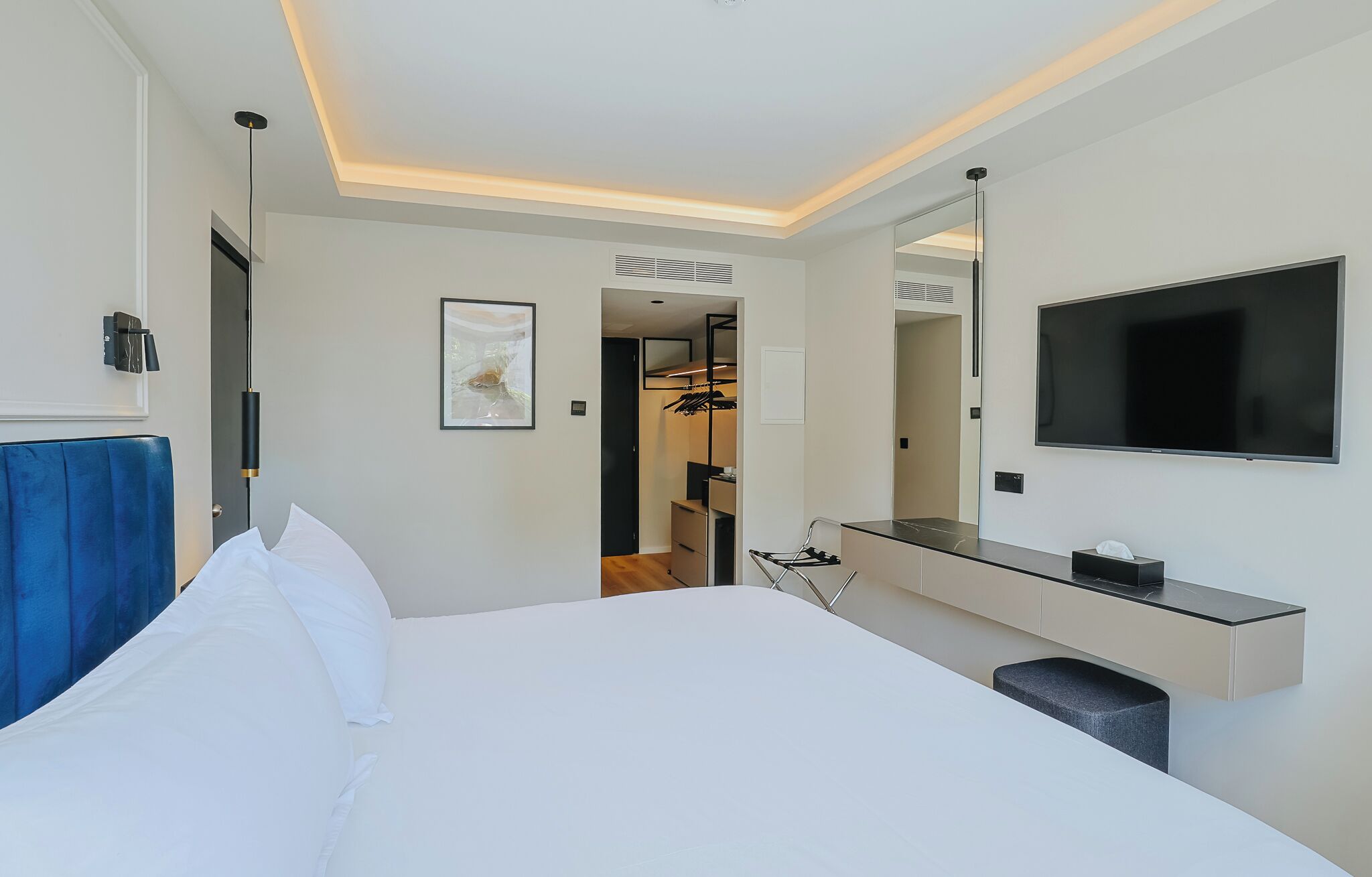 A modern hotel room with a large bed, a TV, a mirror, and a walk-in closet.