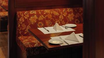 Un asiento de restaurante con una mesa de madera dispuesta para dos personas, incluyendo platos, cubiertos y una servilleta.