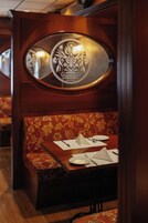 Un asiento de restaurante con una mesa de madera dispuesta para dos personas, incluyendo platos, cubiertos y una servilleta.