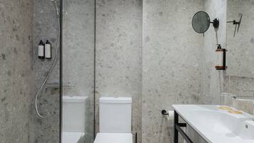 Un baño moderno con ducha envuelta en vidrio, inodoro blanco, lavamanos con espejo y toallero.