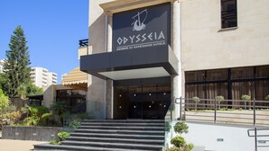La entrada de un hotel llamado 'Odyssea', con un diseño arquitectónico moderno, que presenta un acceso destacado con escalones que conducen a las puertas principales.