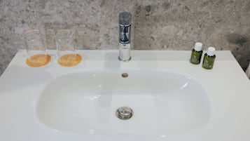 A bathroom sink with a marble backsplash, a chrome faucet, and two small bottles of lotion on the counter.