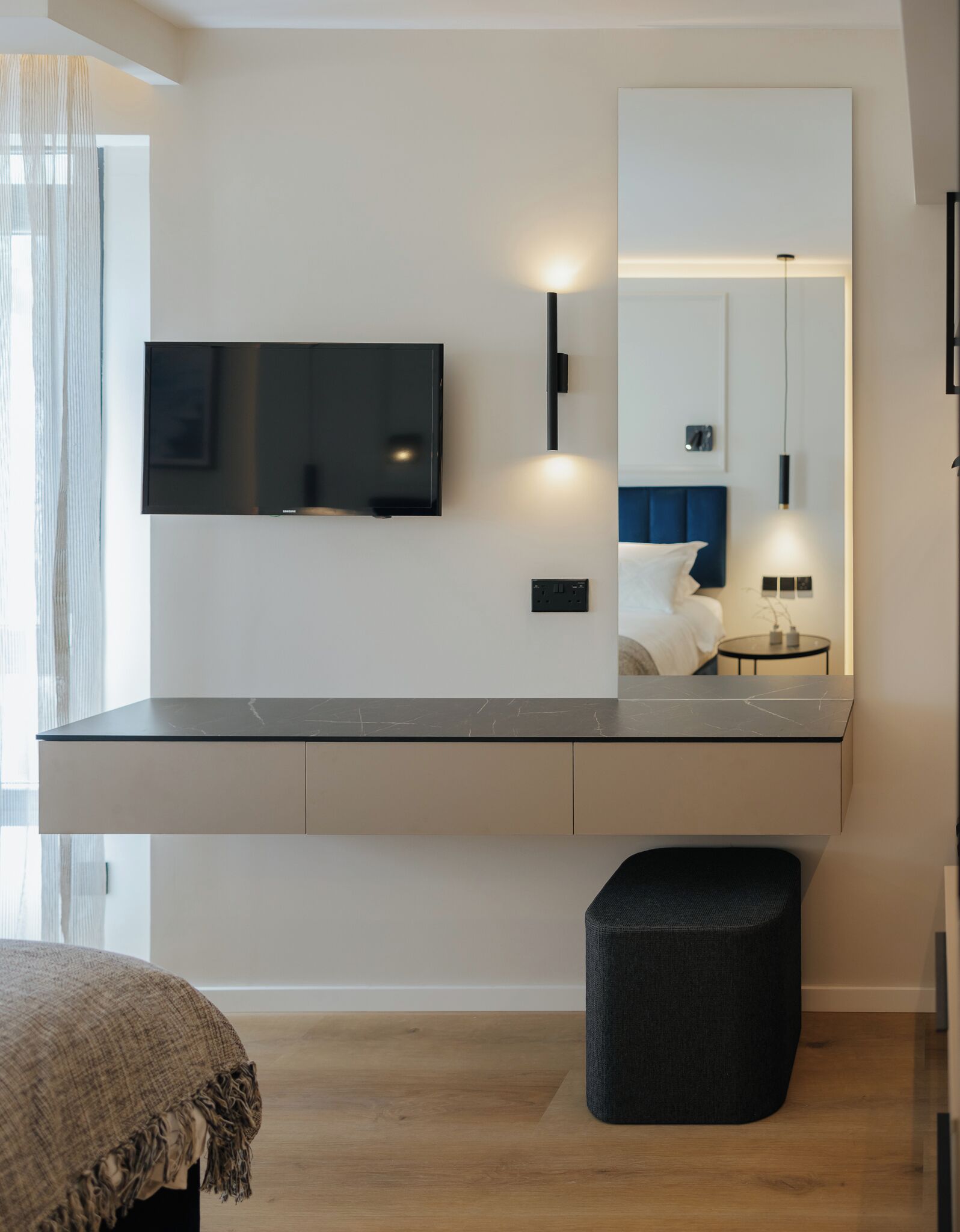 A modern bedroom with a large mirror, a flat-screen TV, and a bedside table.