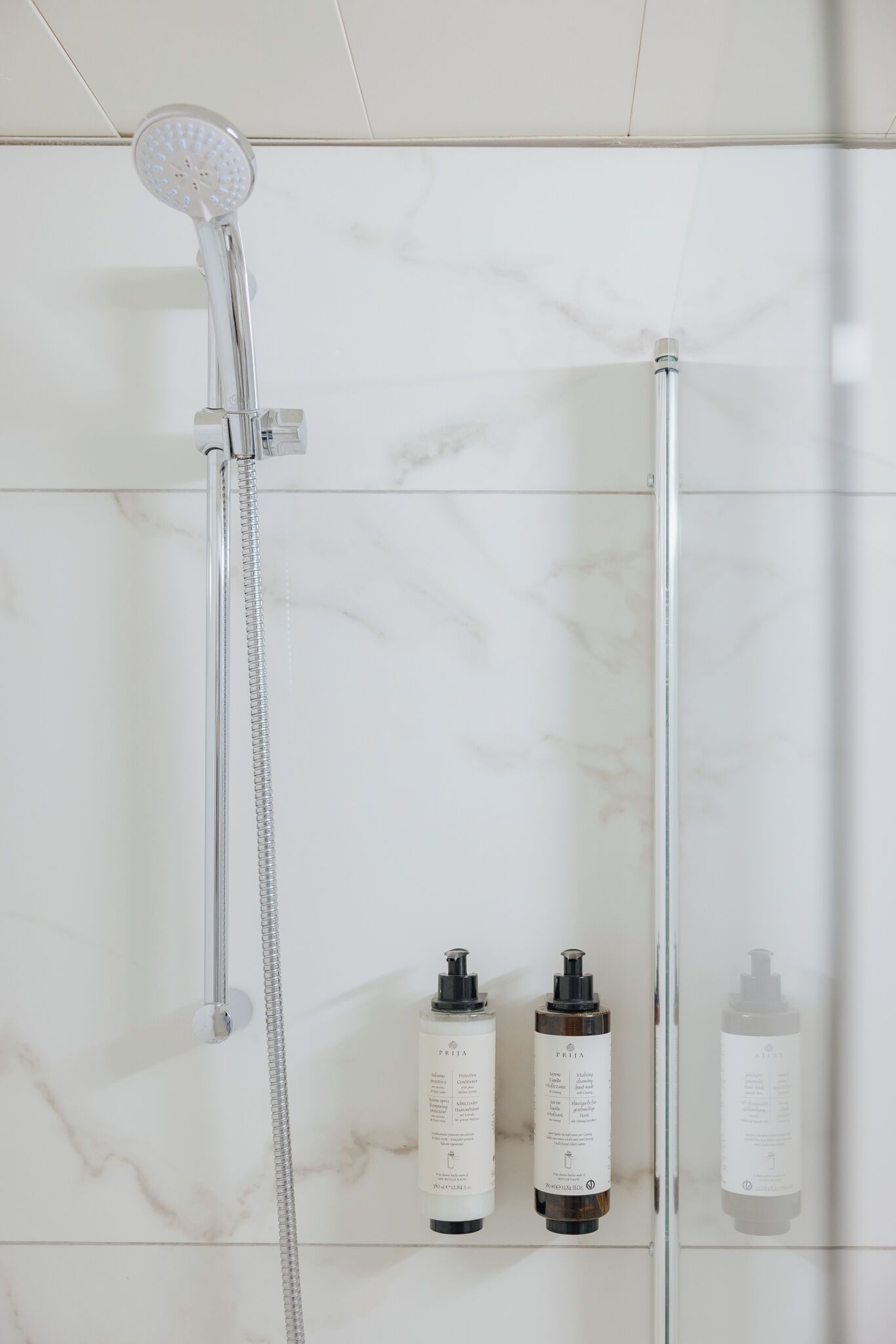 A shower with a handheld showerhead and a glass-enclosed cabinet with three bottles of skincare products.